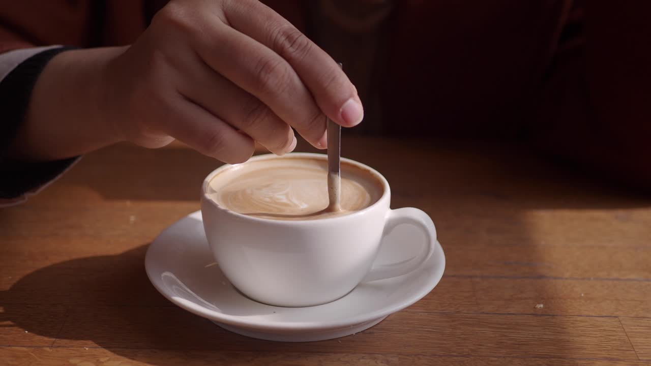 Person stirring a cup of latte art coffee
