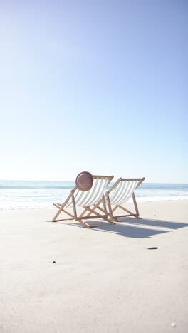 vertical video: two beach chairs with hat on sandy shore, relaxing by ocean