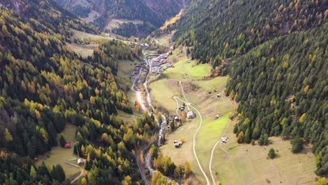 drone flying above swiss village in autumn , fall with mountains and a river on the background