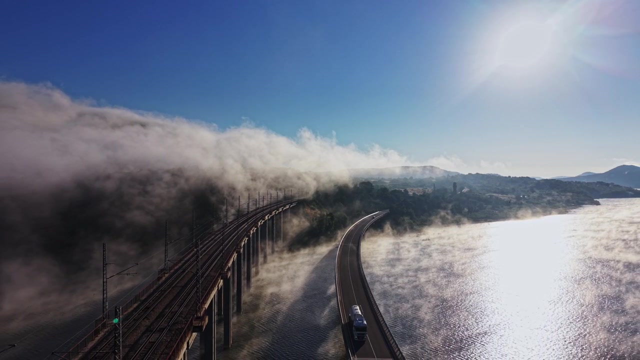 Fog covers bridge and waterway at sunrise with sunlight shining