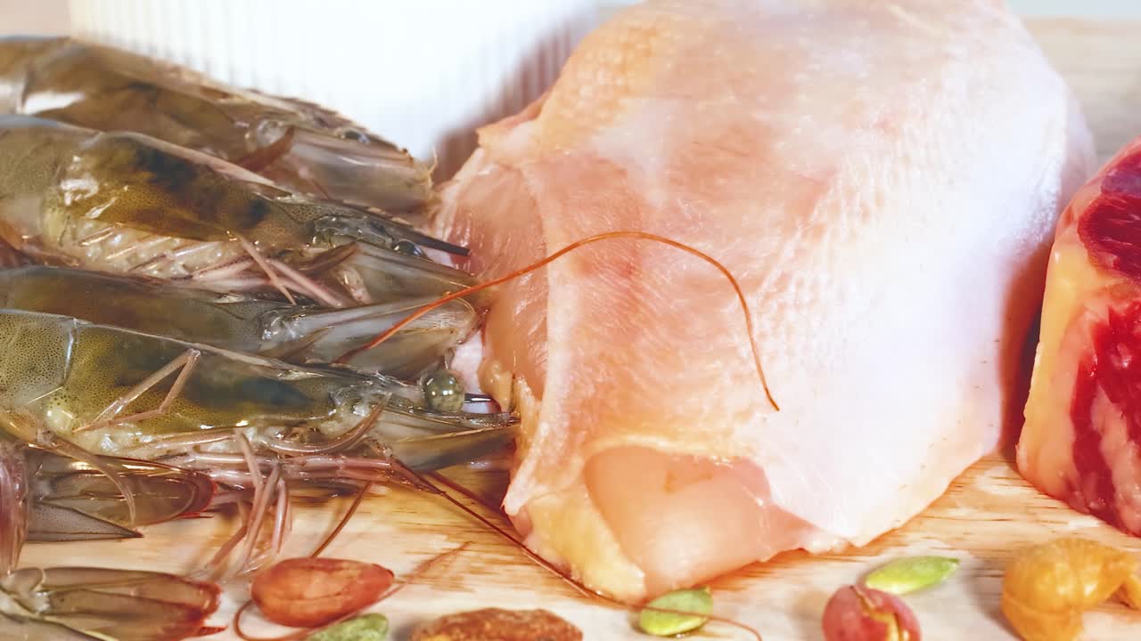 A selection of protein-rich foods including chicken, steak, prawns, eggs, cheese, nuts, and milk on a wooden surface.