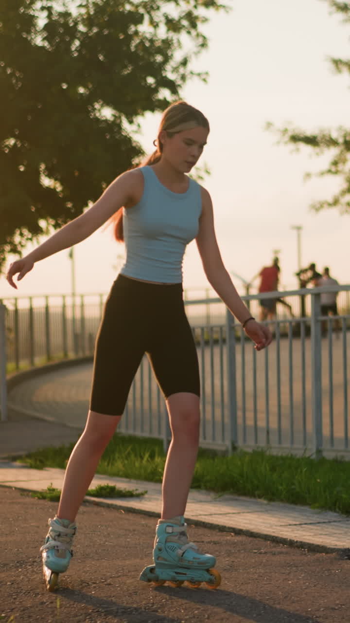 joven patinando al aire libre a lo largo de un camino alineado con barandillas de hierro, manteniendo el equilibrio mientras se mueve bajo el resplandor del atardecer, con el paisaje urbano visible en el fondo borroso y otras personas en la distancia