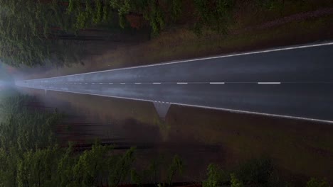 aerial vertical descending shot over the asphalt road in the foggy forest with distant car - horror, dark scenery concept