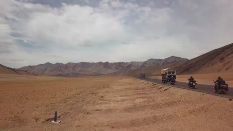 Vista-De-Drones-De-Turistas-En-Moto-Conduciendo-A-Través-De-Las-Montañas-Del-Himalaya-En-India-Con-Tierra-Naranja-Seca-Y-Cielos-Nublados