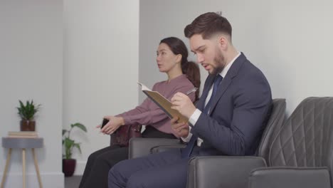 Candidatos-Masculinos-Y-Femeninos-En-El-Cargo-Esperando-Una-Entrevista-De-Trabajo-Mirando-El-Teléfono-Móvil-Y-Leyendo-Notas-3