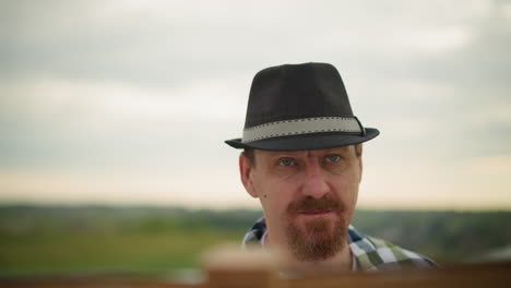 an artist wearing a black hat intensely focused on an unseen task, with mosquitoes visibly flying around his head. a partially visible board in front suggests he's working on something important