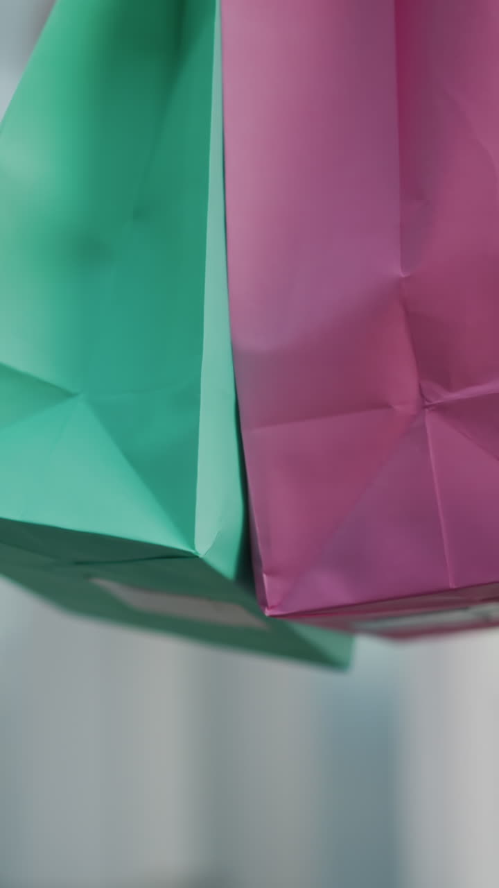 primer plano de bolsas de compras rosas y verdes llevadas por una persona en vaqueros caminando a través de un centro comercial brillantemente iluminado con luces borrosas y colores vibrantes en el fondo