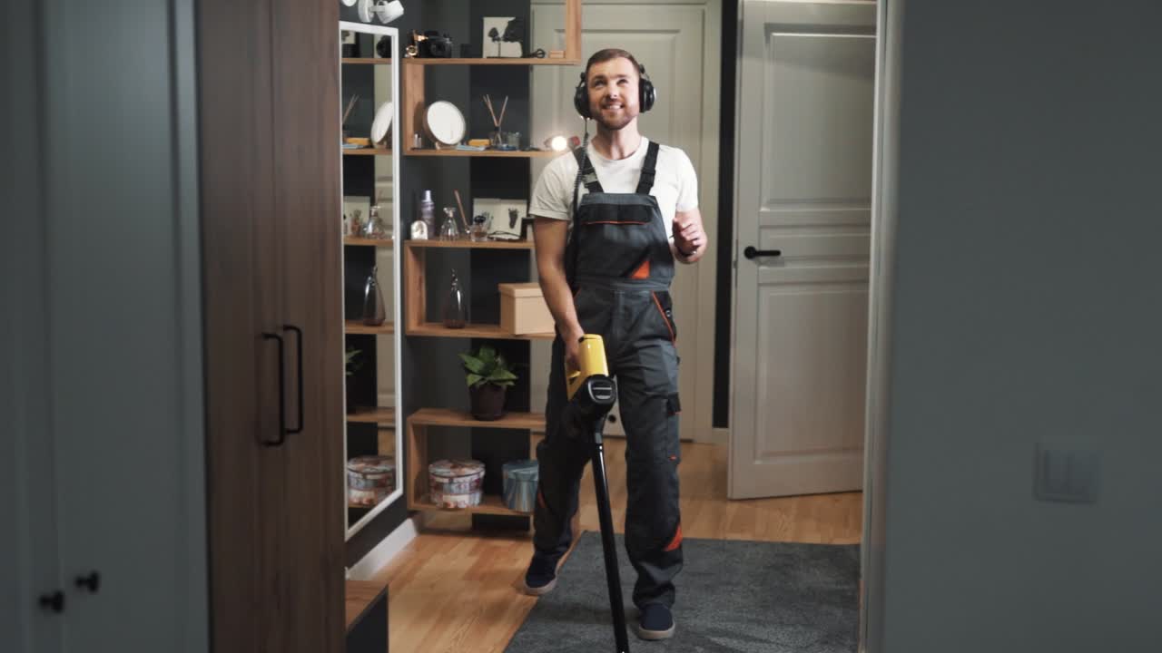 En blid og karismatisk mann i uniform synger og danser mens han rengjør med en trådløs støvsuger