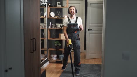 cheerful charismatic man in uniform singing and dancing while cleaning with cordless vacuum cleaner