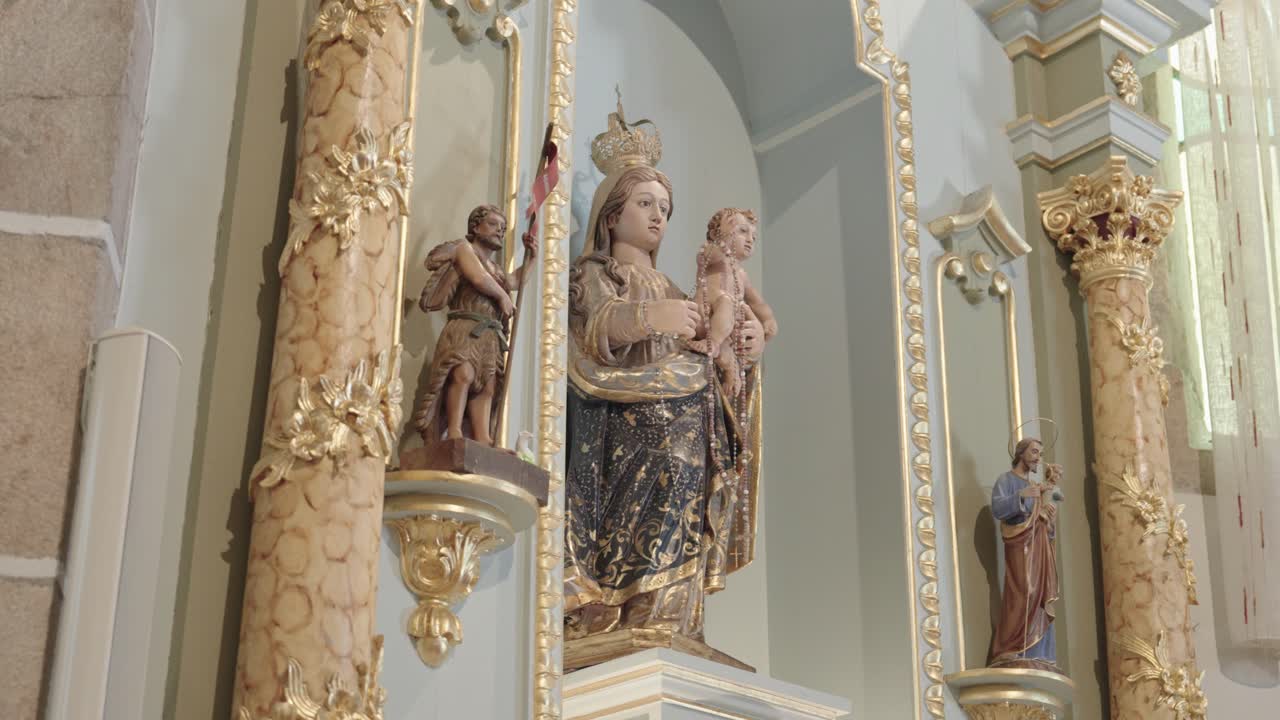 Estátua da Virgem Maria Católica com o Menino Jesus em altar de igreja decorado com colunas e santos.