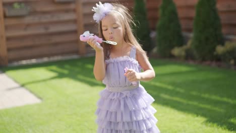 a little girl in a dress is blowing soap bubbles in the backyard on a sunny summer day