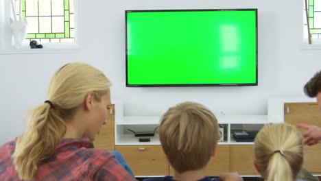 rear view of family sitting on sofa in lounge watching television