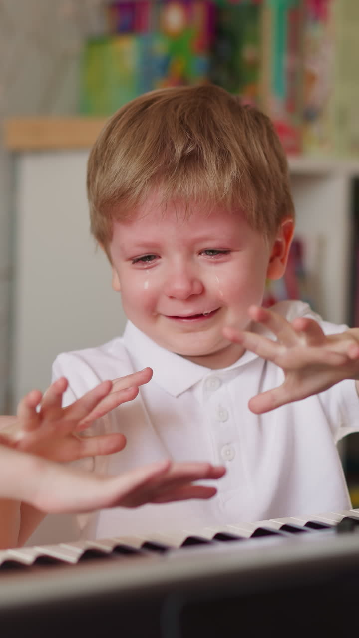 Little girl and boy smiling through tears compare fingers on hands standing near piano in play room. Children take break and have fun during music lesson