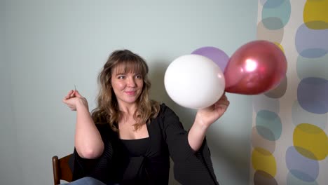 mujer joven sentada en una mesa con las piernas arriba reventando globos