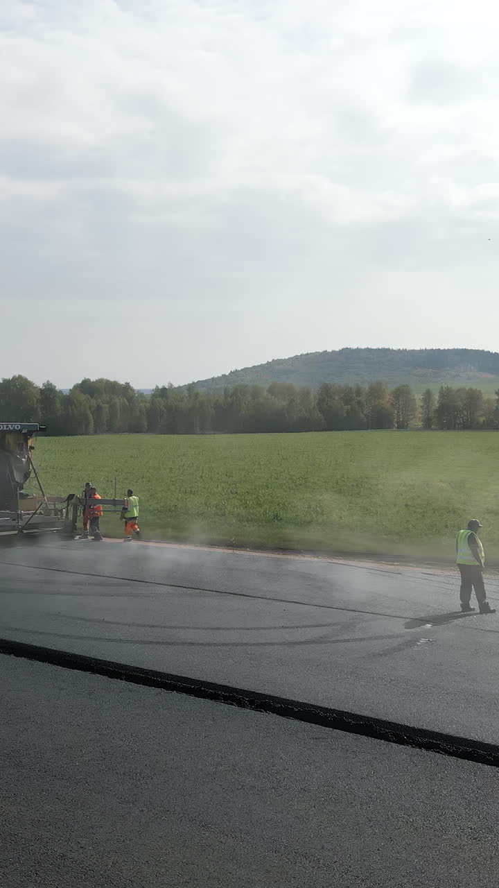 Road construction with asphalt paving machine and workers