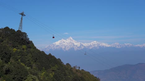 teleféricos que suben y bajan por el tranvía en la ladera de una colina con las montañas del himalaya al fondo