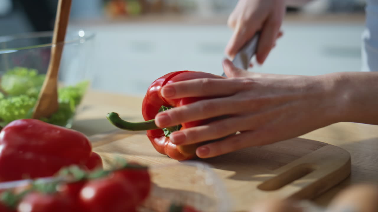 Hands chopping red bell pepper on kitchen countertop closeup. Woman preparing