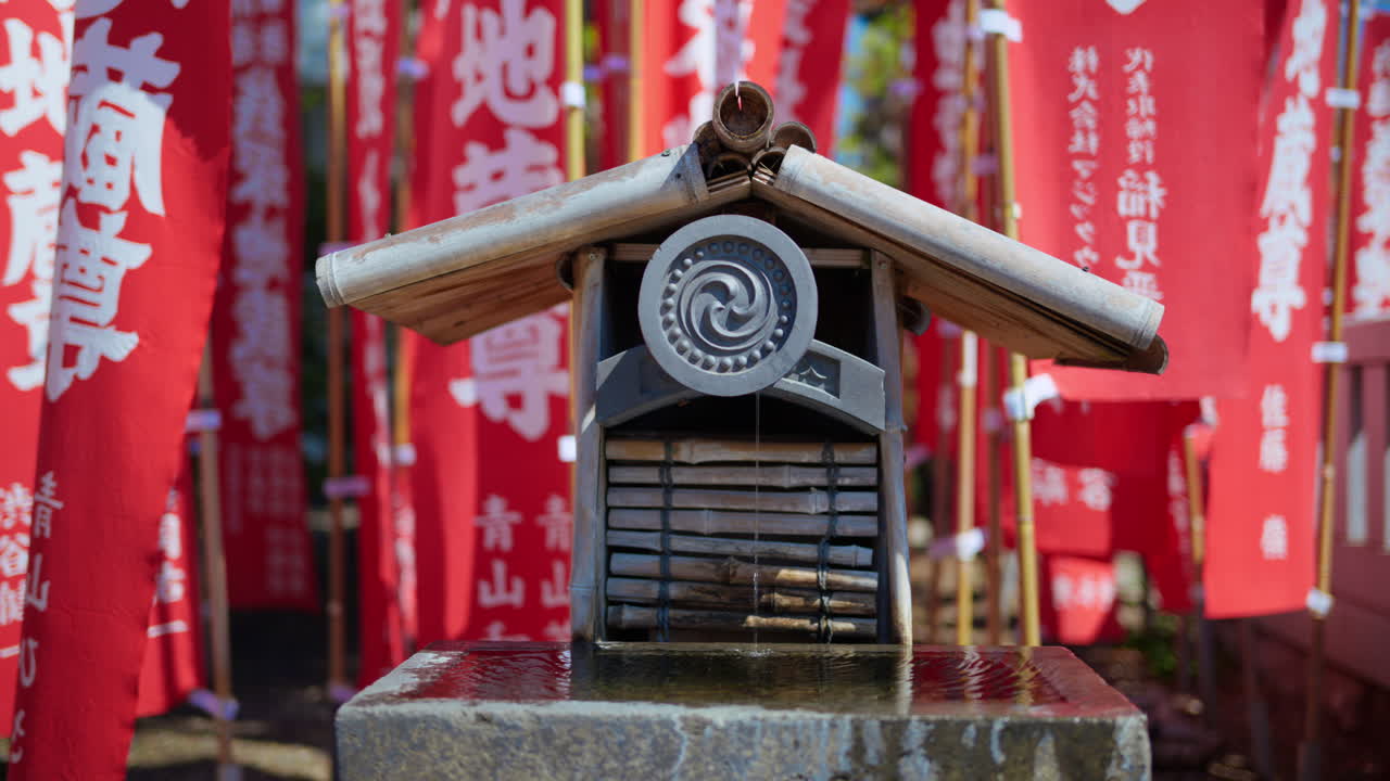 Close up of a small water fountain surrounded by red flags at the Senso-ji temple in Asakusa, Tokyo, Japan. Translation: "Dedication"