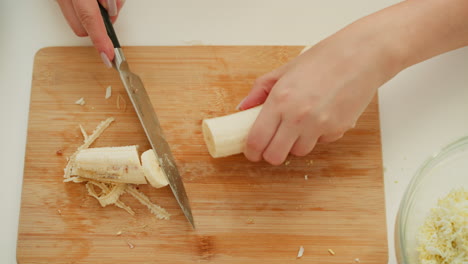 hand view of chef carefully cutting spoiled part of banana on cutting board and slicing remaining portion into tiny round shapes, preparing fresh ingredients in bright, organized kitchen environment