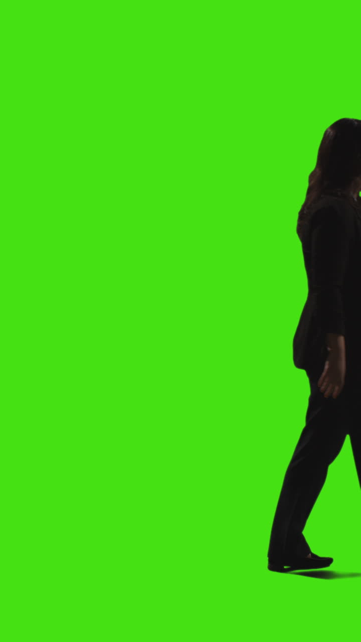 video a vista laterale verticale di una donna d'affari che parla al cellulare che cammina attraverso la cornice contro lo schermo verde
