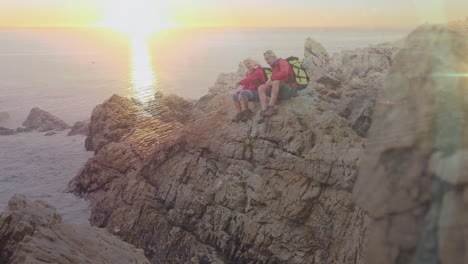 caucasian senior couple hiking in countryside sitting on rocks talking, with sunsetting over sea