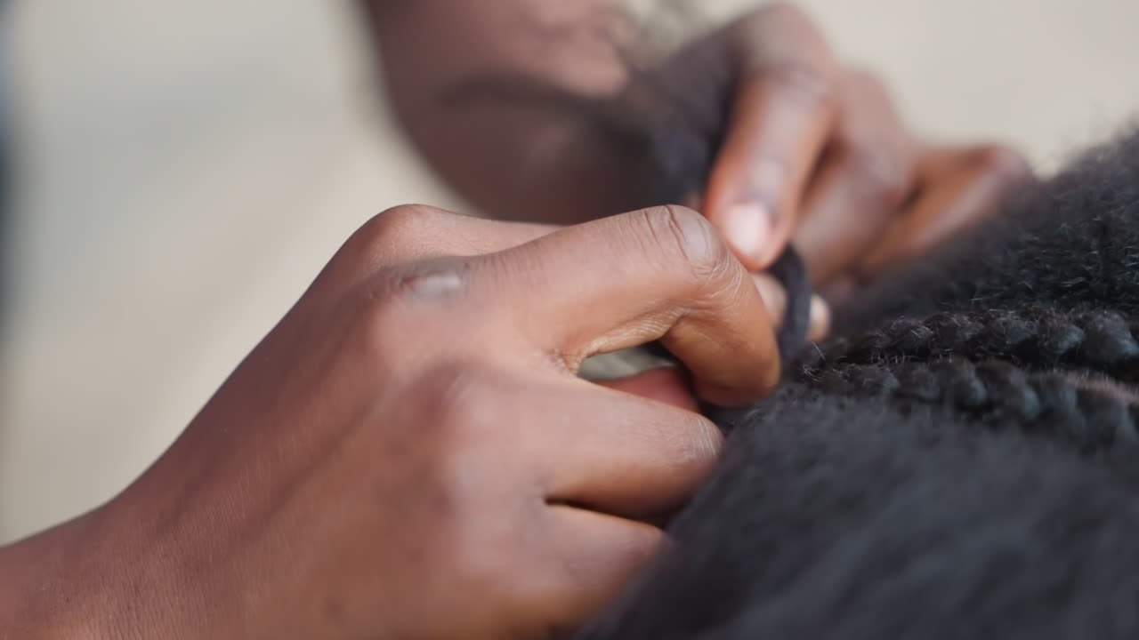 Primo piano di una trecciatrice nera che crea cornrows con dita precise, separazioni nette e dritte e movimenti ritmici delle mani. Acconciatura tradizionale in un ambiente di salone concentrato, con un look finale elegante che emerge.