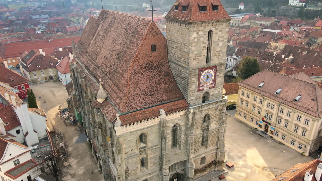 Dronebillede i fugleperspektiv af Den Sorte Kirke i det gamle centrum af Brasov, Rumænien. Gamle beboelsesejendomme omkring kirken, bakker med grønne områder.
