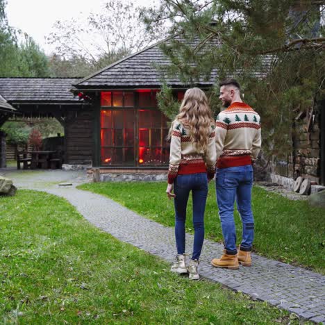 young couple in the village. handsome man and beautiful girl in christmas sweaters are running in the yard of cottage. romantic couple enjoying life outdoors.