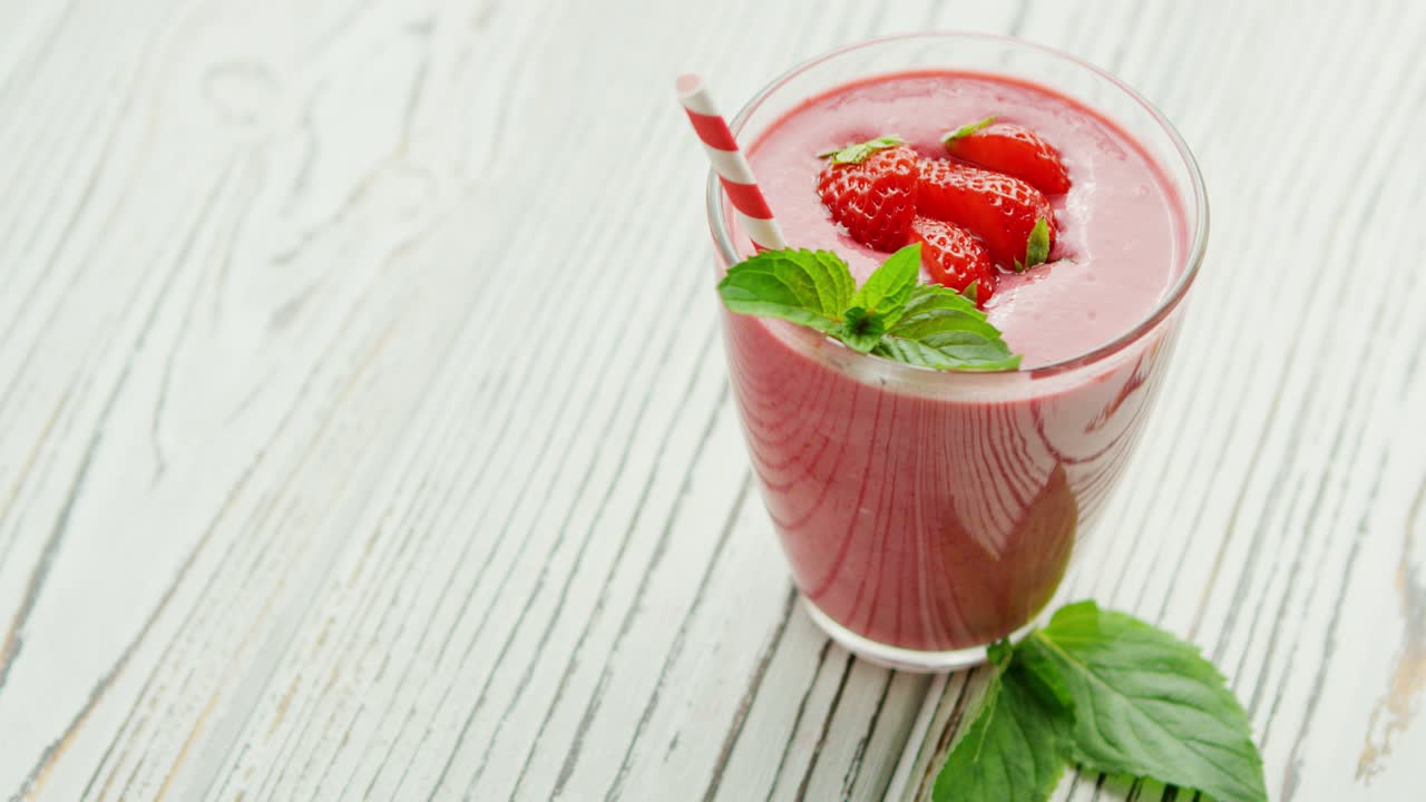 Glass with smoothie and bowl of strawberries