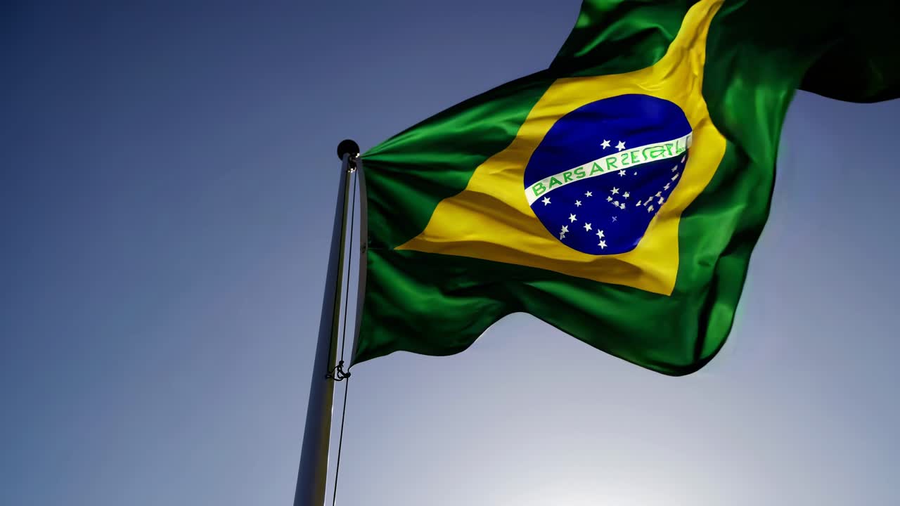 Inquadratura dal basso della bandiera brasiliana che sventola contro un cielo sereno, catturando un senso di orgoglio
