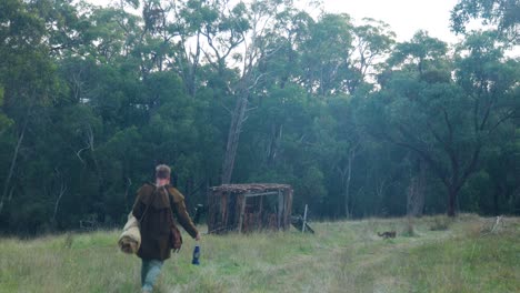 a bushman walking to a historical bark hut in the australian bush