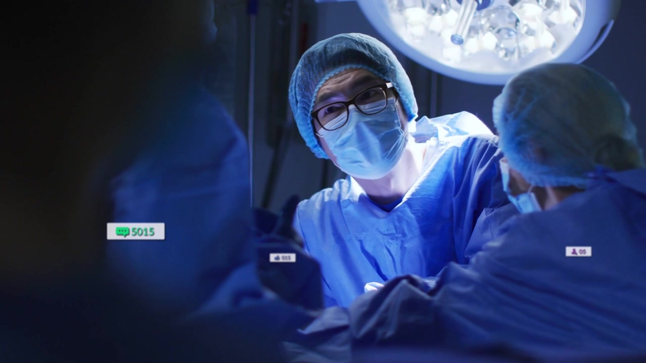 Chirurg manipulující skalpelem pod lampou, živý přenos způsobuje narůstání indikátorů pro monitorování.