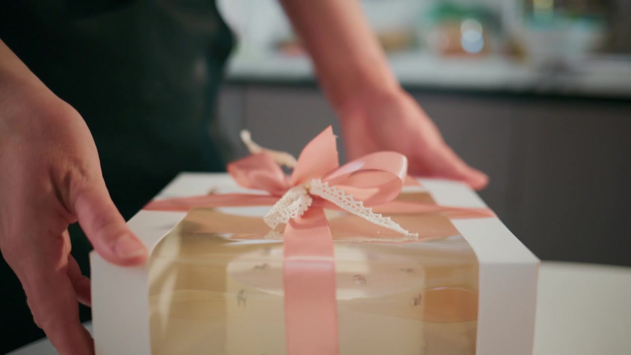 Manos atan cuidadosamente un lazo rosa en una caja de regalo. Dedos concentrados ajustan el lazo con suave precisión. La iluminación suave resalta el delicado proceso de envoltura. Ideal para festividades, celebración.