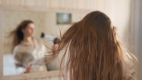 beautiful young woman blow-drying her hair in front of a mirror