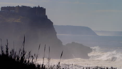 welle bricht gegen die klippe in nazare, portugal unterhalb des leuchtturms