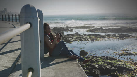 animación de una mujer biracial sonriente tomando una foto con una cámara en el paseo marítimo