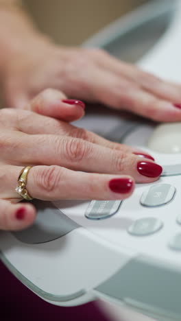 adult female hands with red manicure and ring manage the buttons on the equipment panel. close up. medic working on ultra sound machine.