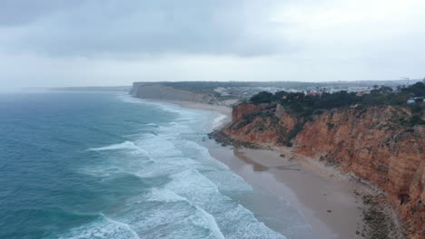 Increíble-Vista-Aérea-De-Drones-De-La-Playa-De-Arena-De-Lagos-Con-Olas-Rompiendo-Contra-La-Costa,-Día-Nublado,-Muñeca-En