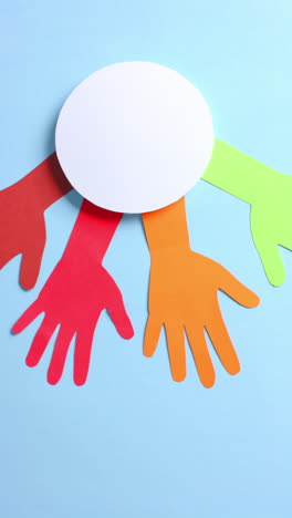 vertical video of hands around circle made of colourful paper on blue background with copy space