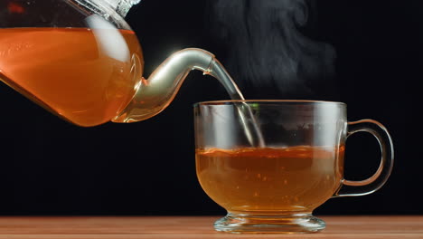 hot tea being poured from a glass teapot into a clear glass cup, with steam rising