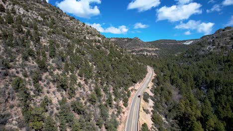 Car-drives-up-two-lane-mountain-pass-in-spring-with-pine-trees-and-blue-Skies-with-clouds