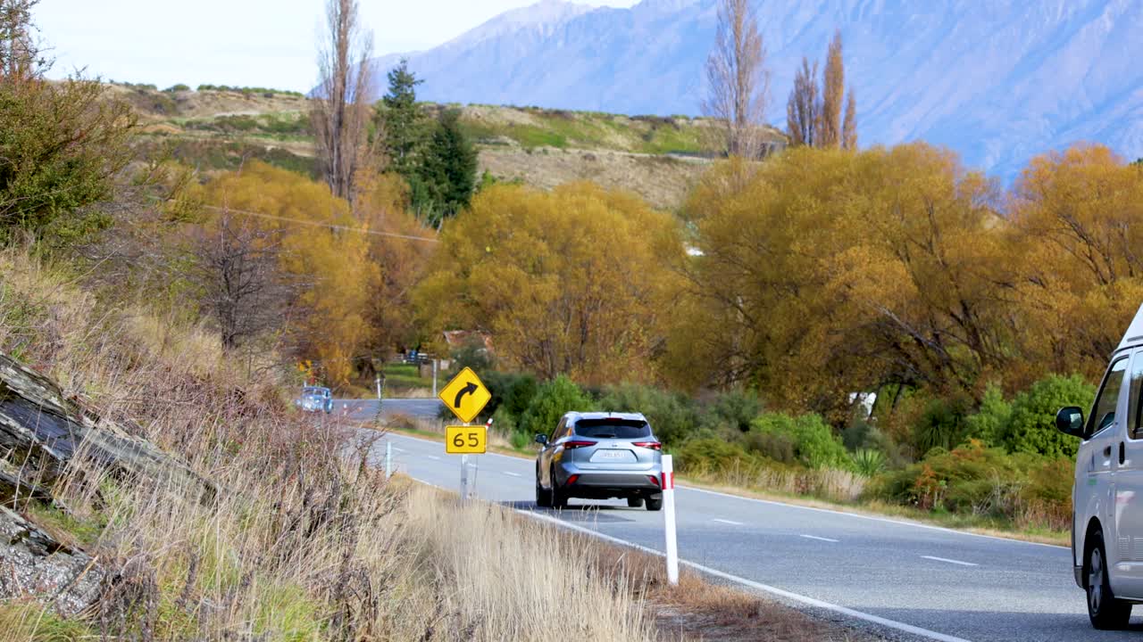 Vehicles travel a winding road amidst lush landscapes and mountains, captured in bright daylight with clear skies