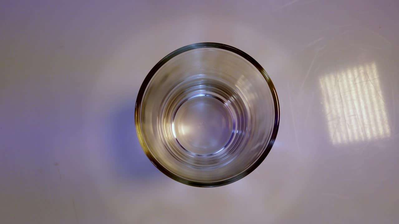 Top-down zenit zoom ud af et transparent, tomt glas på en flad overflade