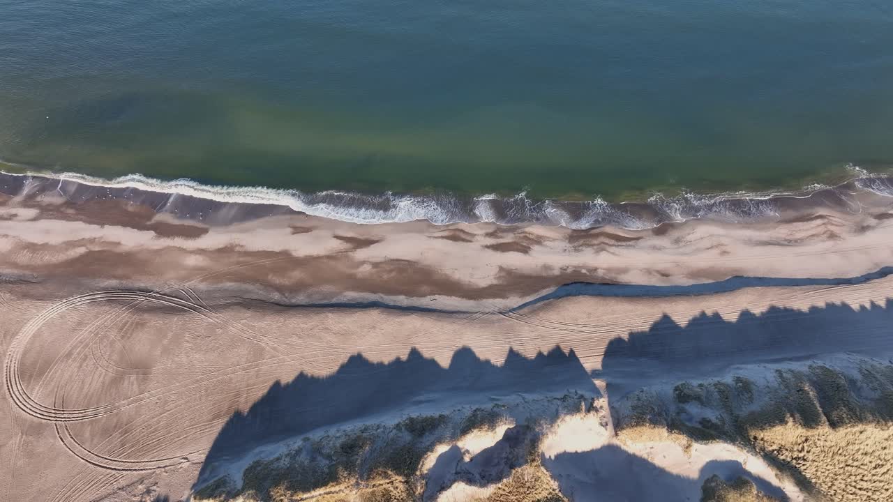 A drone films a peaceful North Sea beach lined with sand dunes. The image is stable and clear, capturing the quiet beauty of the empty shoreline with no people in sight.