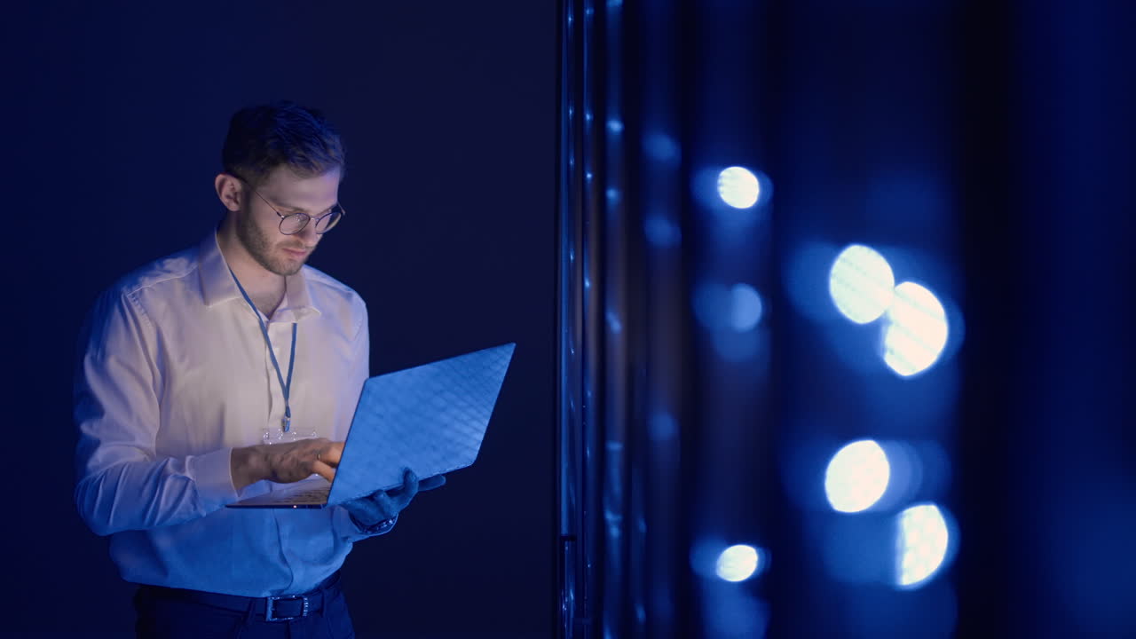 Male Server Engineer in Data Center. IT engineer inspecting a secure server cabinet using modern technology laptop coworking in data center.