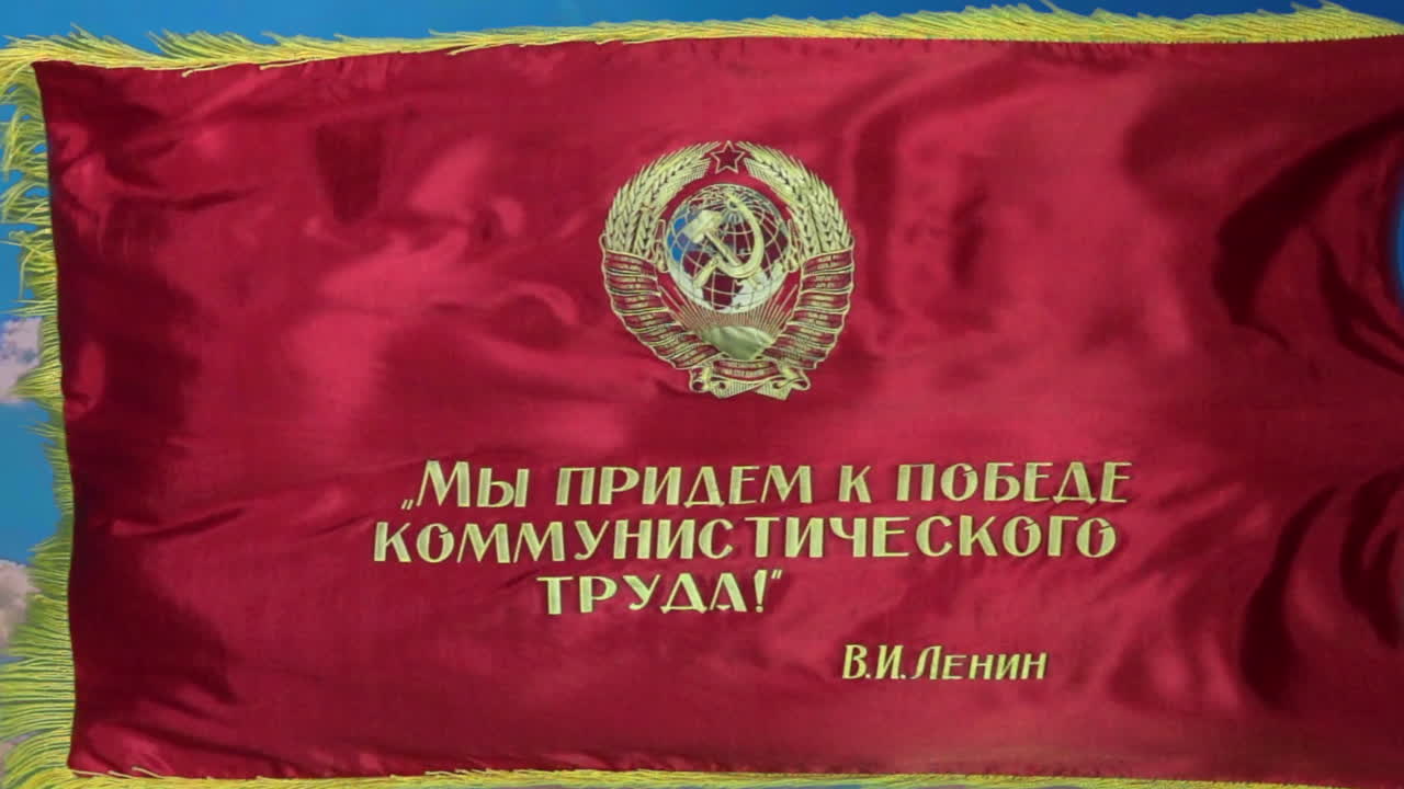 Zoom in on Soviet parade flag with hammer and sickle emblem flying in slow motion with vivid blue sky in background