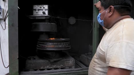 mecánico latino marrón que usa una máscara bucal para protegerse mientras espera una máquina de repavimentación de rotor para volantes en el taller automotriz
