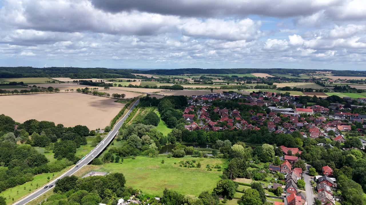 Rural road of historic town in Germany during sunny day with clouds. Agricultural farm fields and hills in distance. Red tile roof houses in small town of America. Aerial wide shot