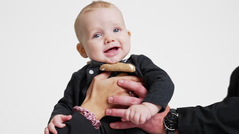 male and female hands hold beautiful smiling caucasian infant. mother and father kiss their lovely son on the head. white backdrop.