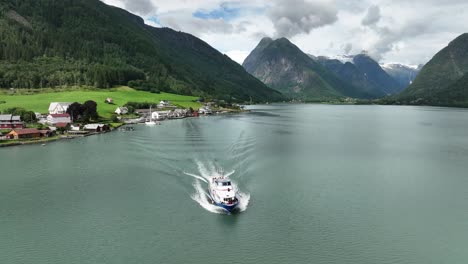 Barco-Turístico-Partiendo-De-Fjaerlandsfjorden-Con-Aldea-Y-Glaciar-Boyabreen-Visto-En-El-Paisaje-De-Montaña-De-Fondo